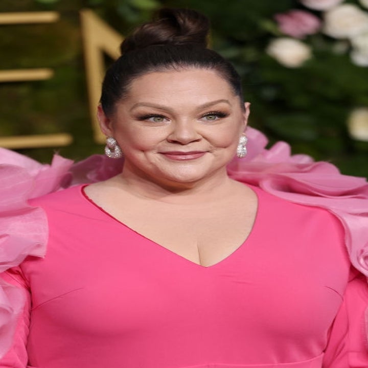 Actress in a flowing gown with large ruffled sleeves attends a red carpet event, smiling and wearing statement earrings