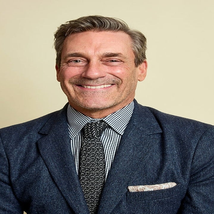 Smiling man in a checkered shirt and suit jacket poses against a plain background