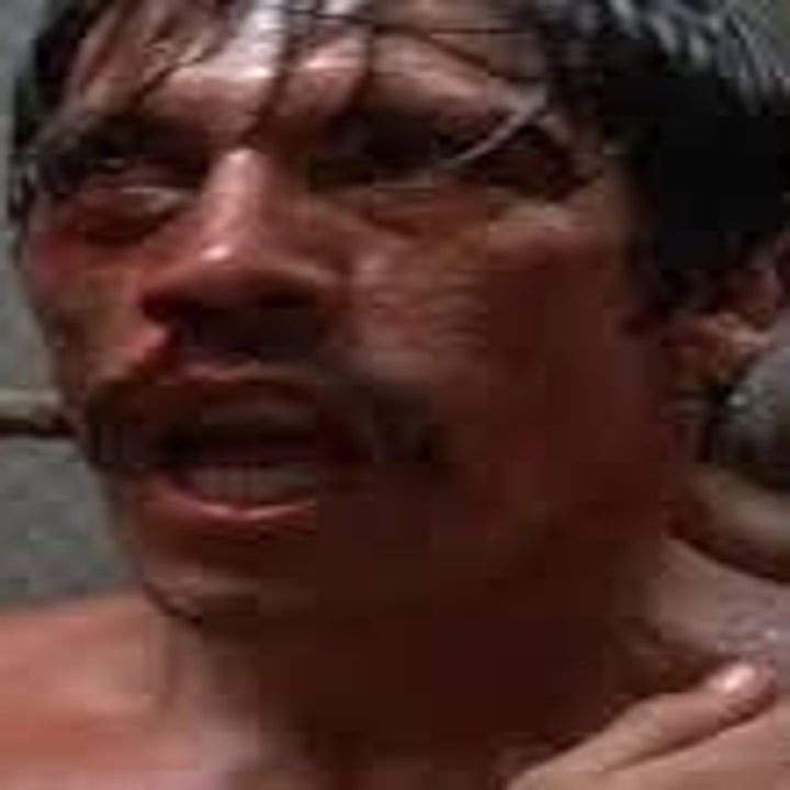 A man in a boxing ring, appearing exhausted and sweaty, with two others attending to him