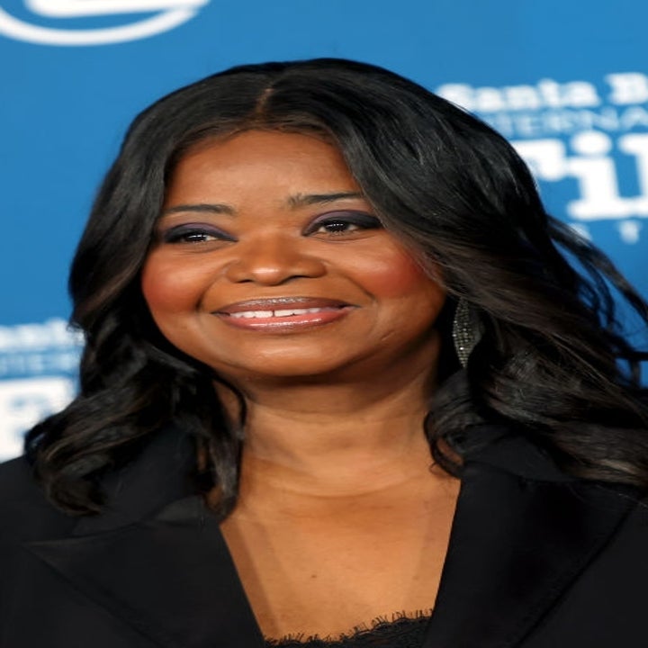 Person in a formal black blazer at a film festival event, smiling against a backdrop with film-related logos