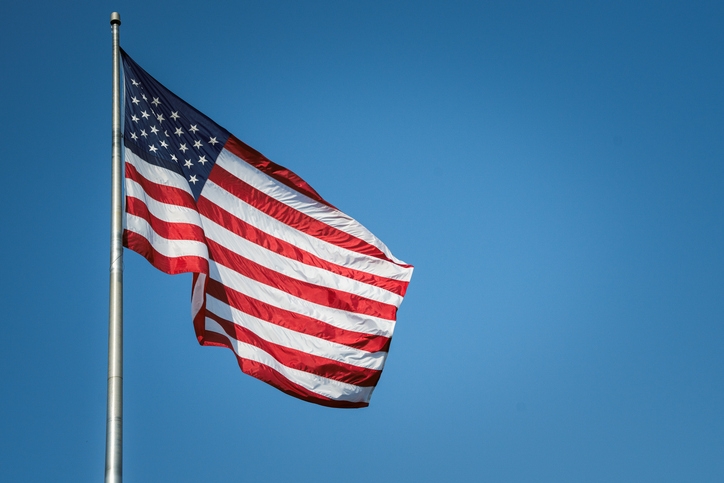The image shows an American flag waving on a flagpole against a clear sky