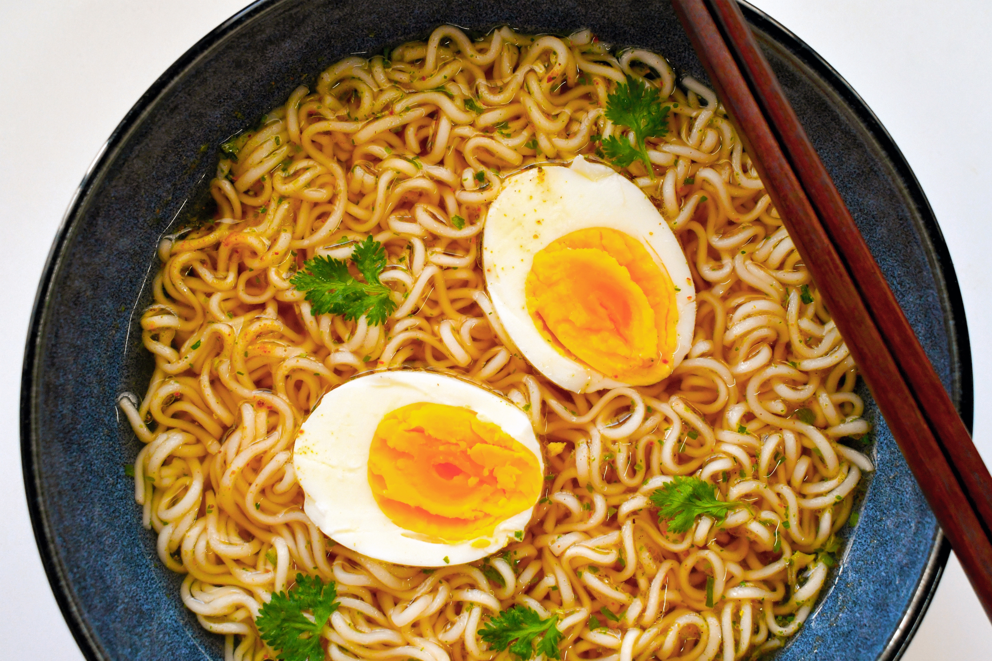 Bowl of ramen with sliced boiled eggs, parsley, chopsticks, and a flavorful broth