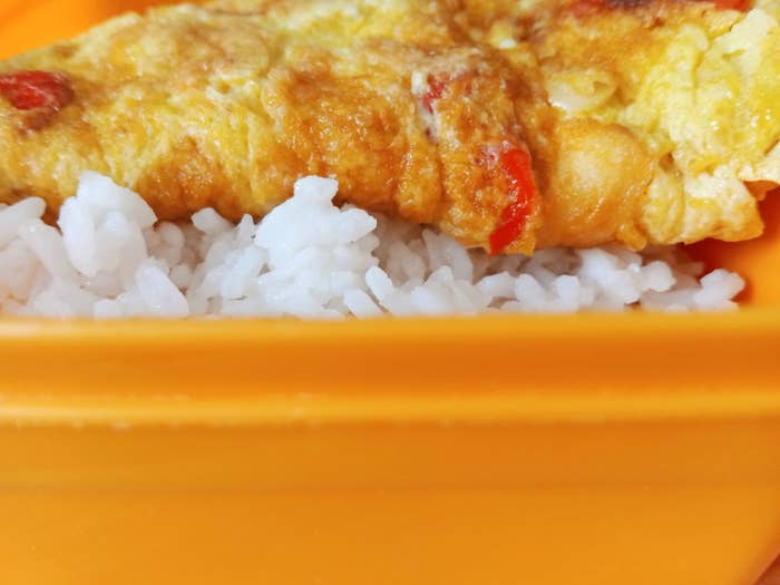 Omelette with vegetables served over white rice in an orange container