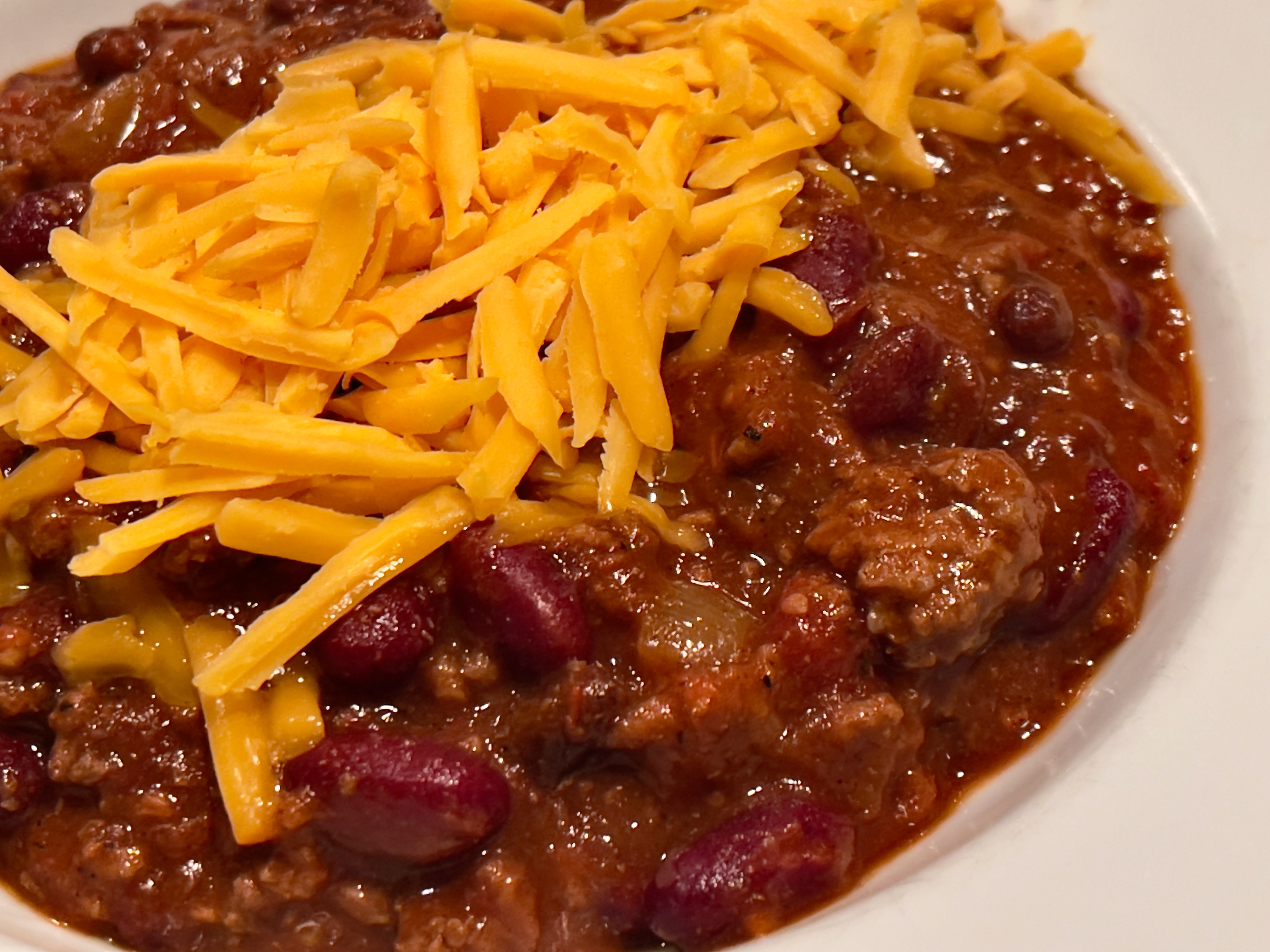 A bowl of chili topped with shredded cheddar cheese, beans, and ground meat