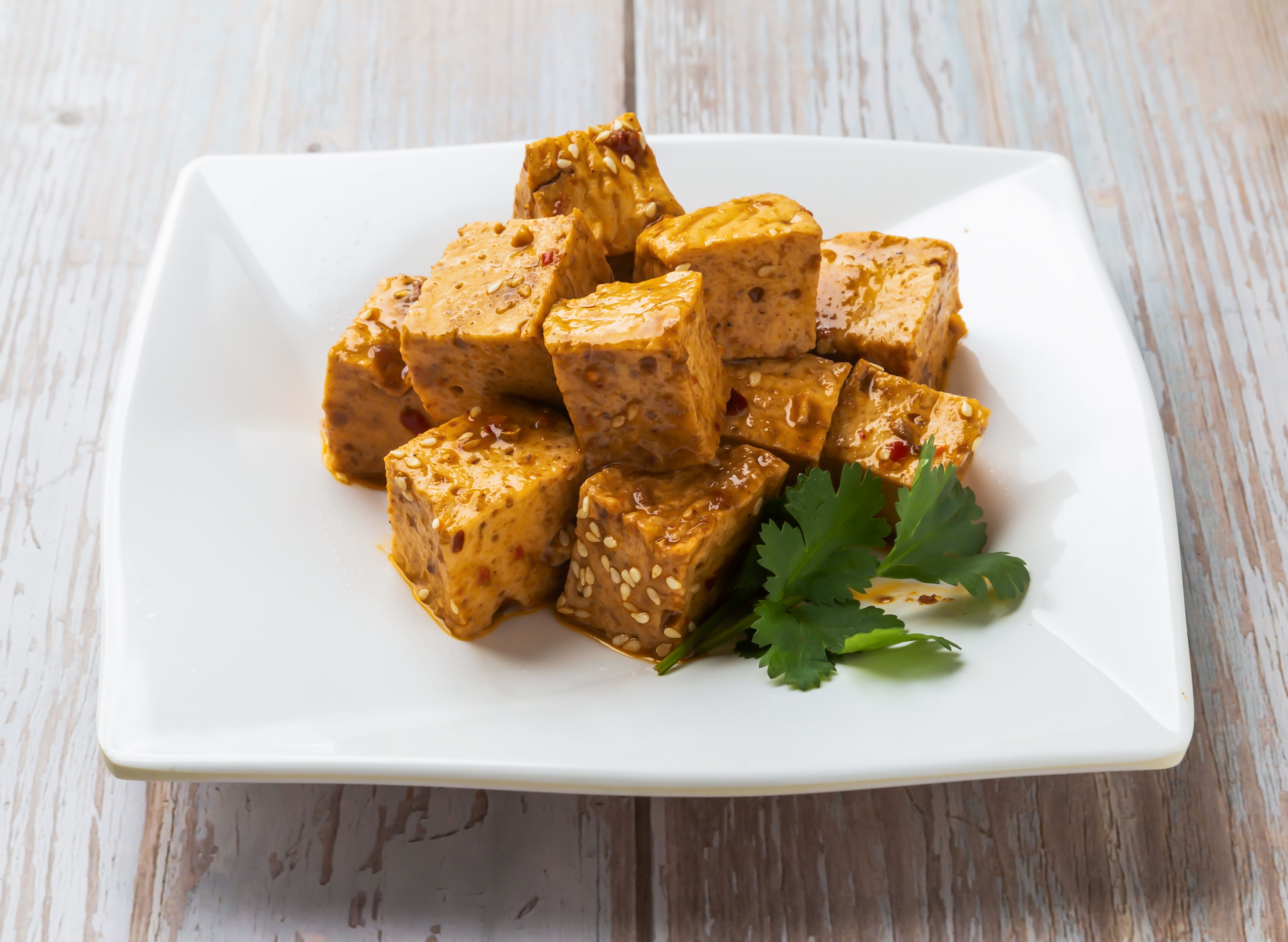 Cubes of marinated tofu garnished with sesame seeds and cilantro on a square white plate