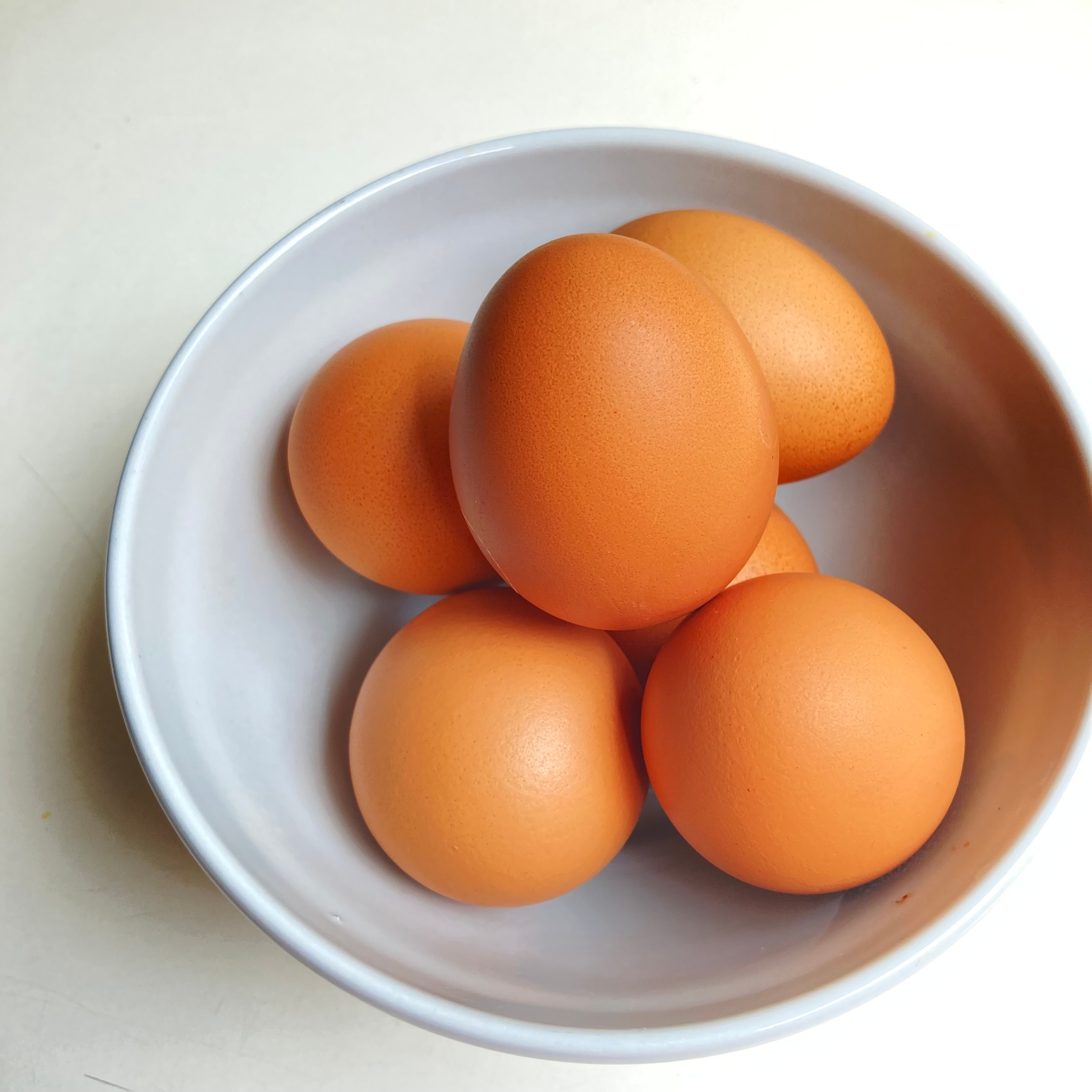 A white bowl containing six brown eggs