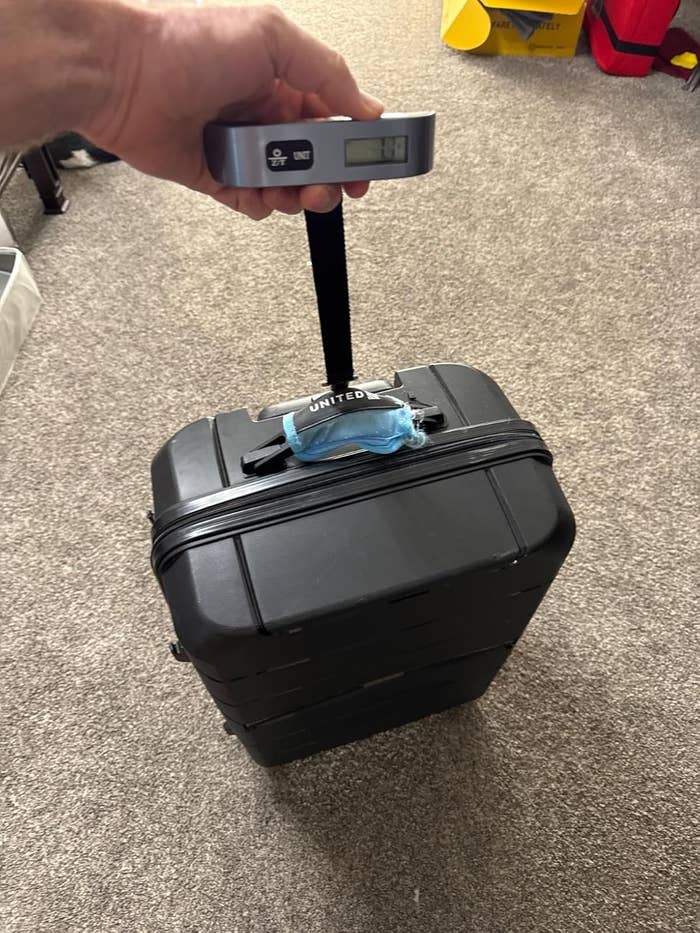 A manus holds a integer luggage standard measuring the value of a tiny rolling suitcase connected carpeted flooring.