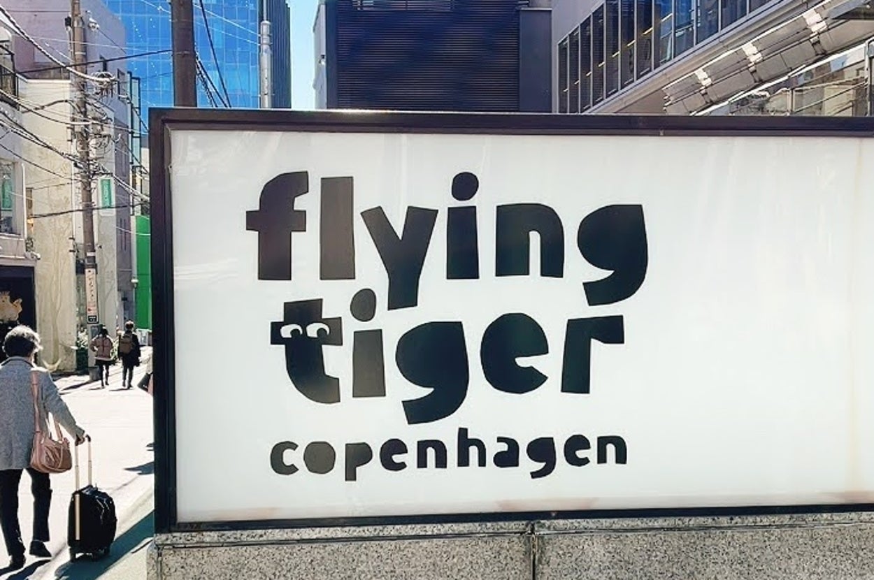 デンマーク発の雑貨店「Flying Tiger Copenhagen」の看板。通りを歩く人々が背景に映る都市の風景。