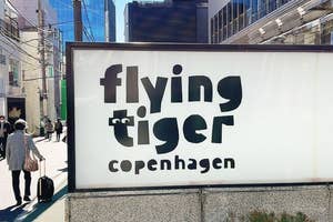 デンマーク雑貨店「Flying Tiger Copenhagen」の看板が都会の通りに設置されています。歩道には歩行者がいます。