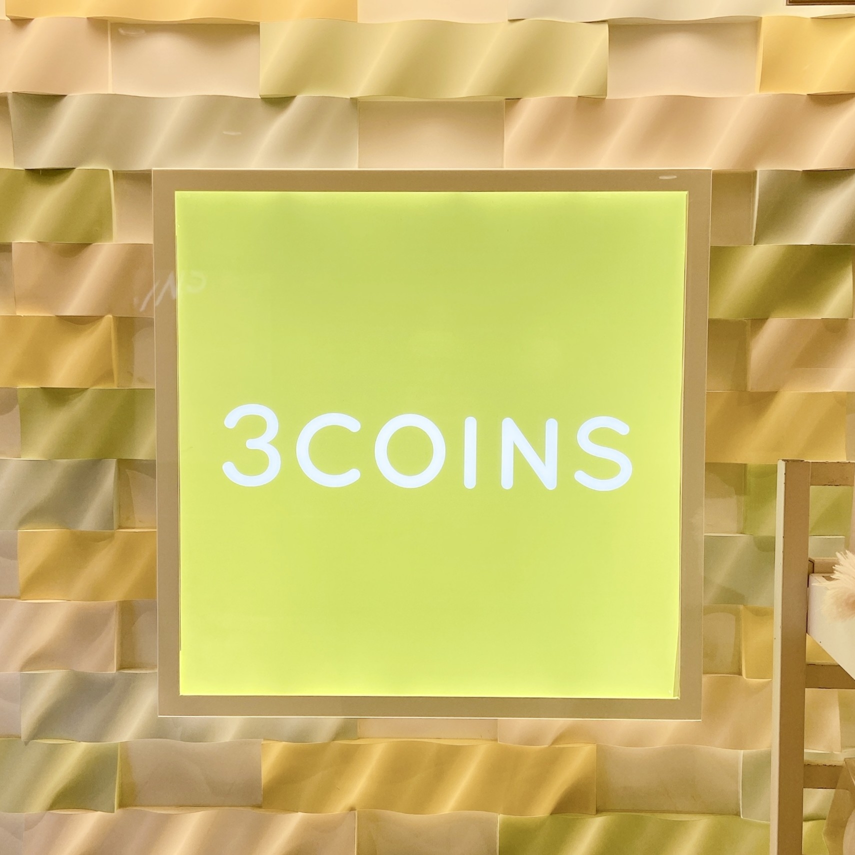 「3COINS」のロゴが中央に配置された広告画像。背景はシンプルで立体感がある。