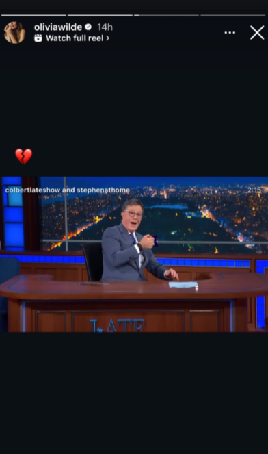 Late-night host in suit gestures at desk during show. Image tagged with &#x27;colbertlateshow&#x27; and &#x27;stephenathome&#x27;. Red broken heart emoji added