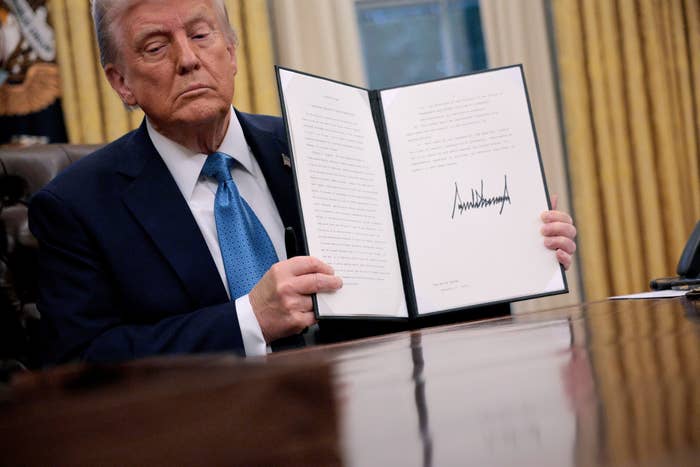 A person at a desk shows a signed document to the camera, holding it open with both hands