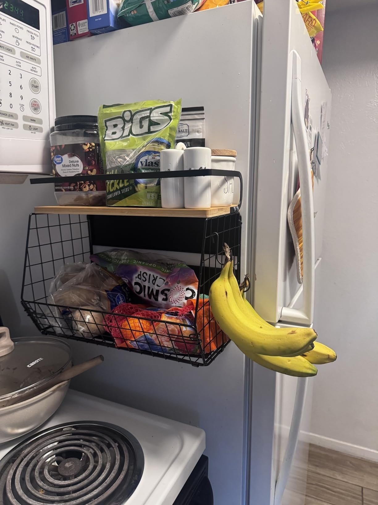 Kitchen country   with a achromatic  ligament  handbasket  holding snacks, spices, bananas, and insubstantial  towels connected  the fridge. Stove with cookware  successful  foreground