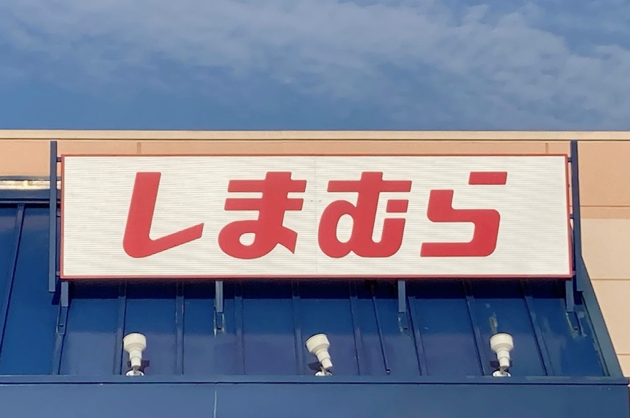 Storefront with a sign in Japanese characters, reading "Shimamura," over the entrance. Blue awning and a wheelchair-accessible parking sign visible