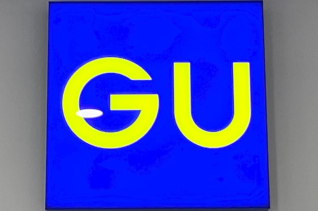 Illuminated sign displaying large yellow letters "GU" on a blue background