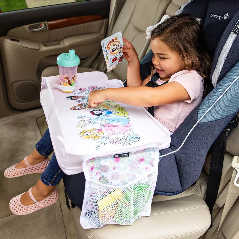 Child sitting in a car seat using a tray with a princess design, eating snacks, and holding a drink in a spill-proof cup