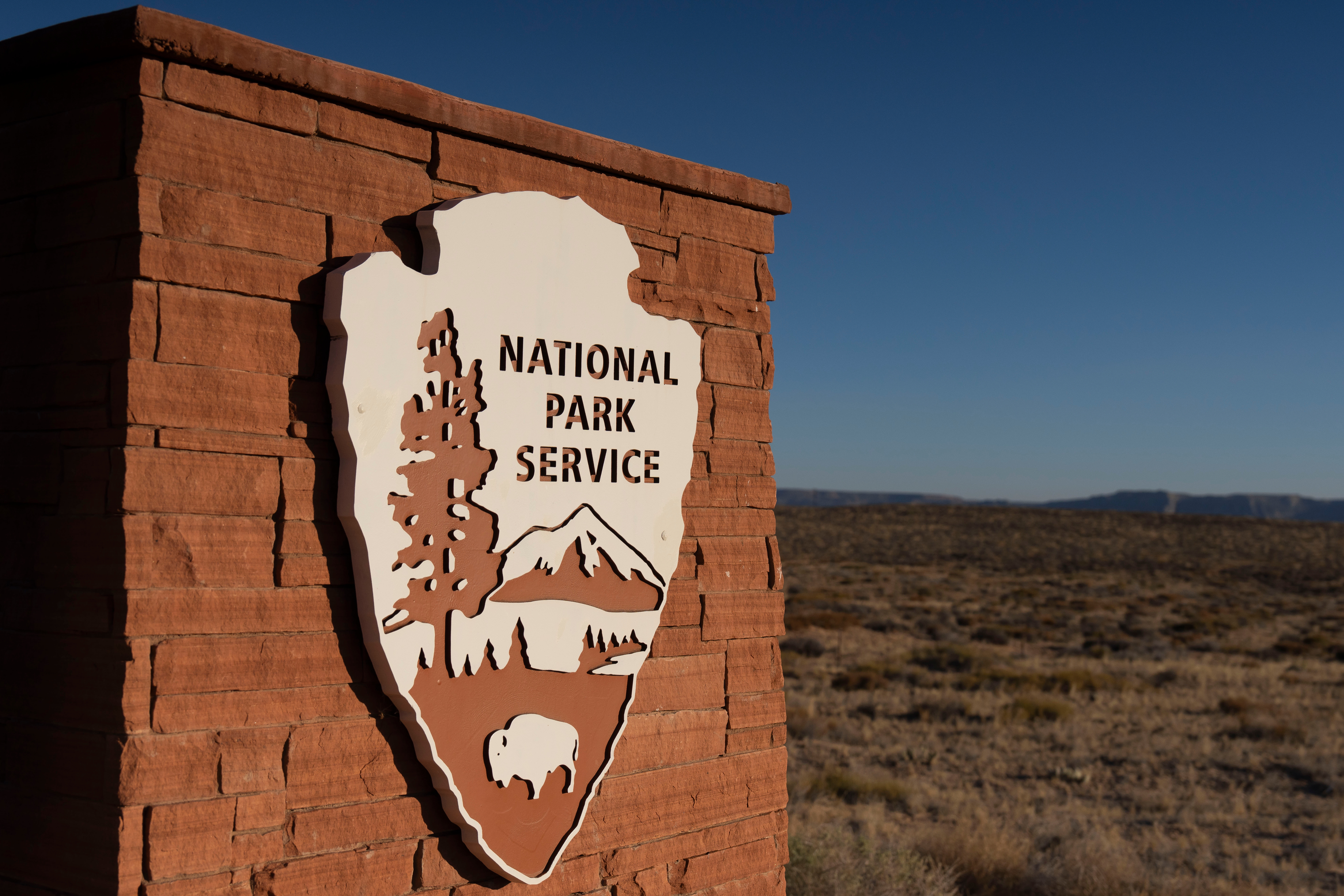 National Park Service shield logo on a stone sign in a vast desert landscape