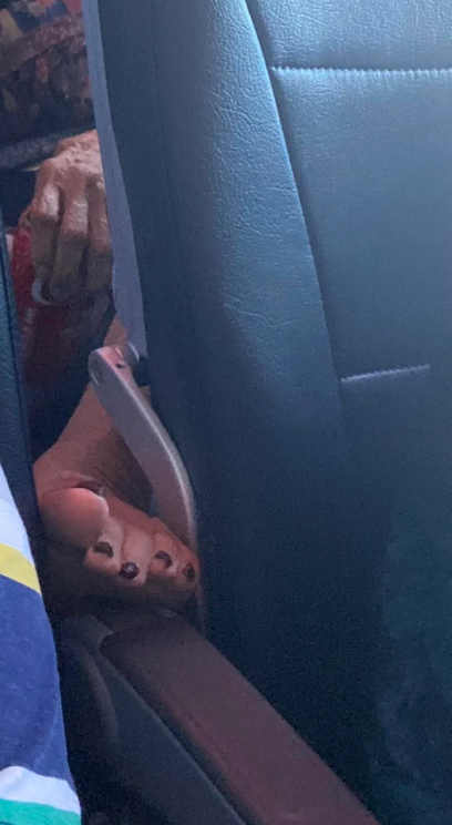 A person&#x27;s foot with painted toenails is resting on an airplane seat armrest
