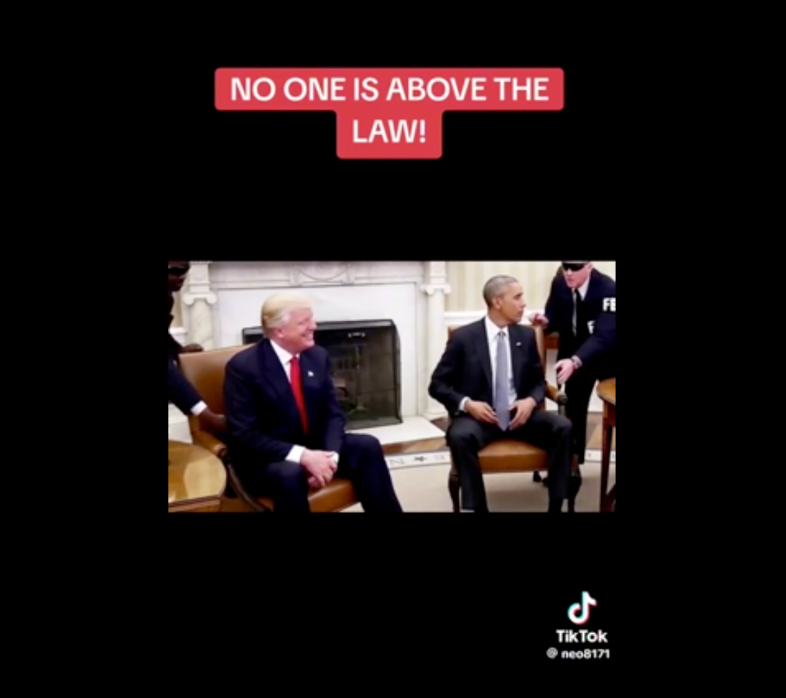 Two men in suits seated in a formal room with a banner above reading &quot;No one is above the law!&quot;