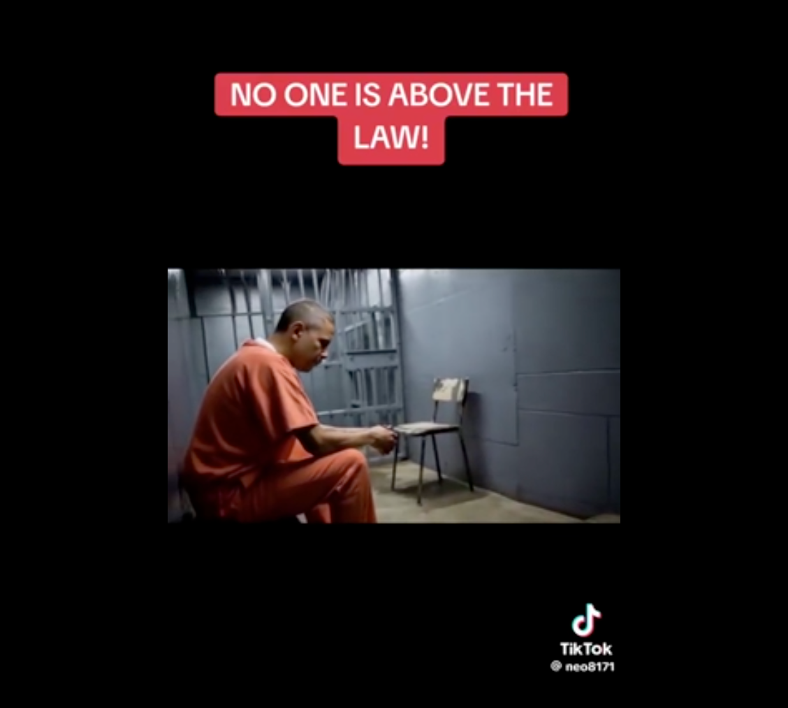 A person in an orange jumpsuit sits in a jail cell looking down. Text above reads, &quot;No one is above the law!&quot;