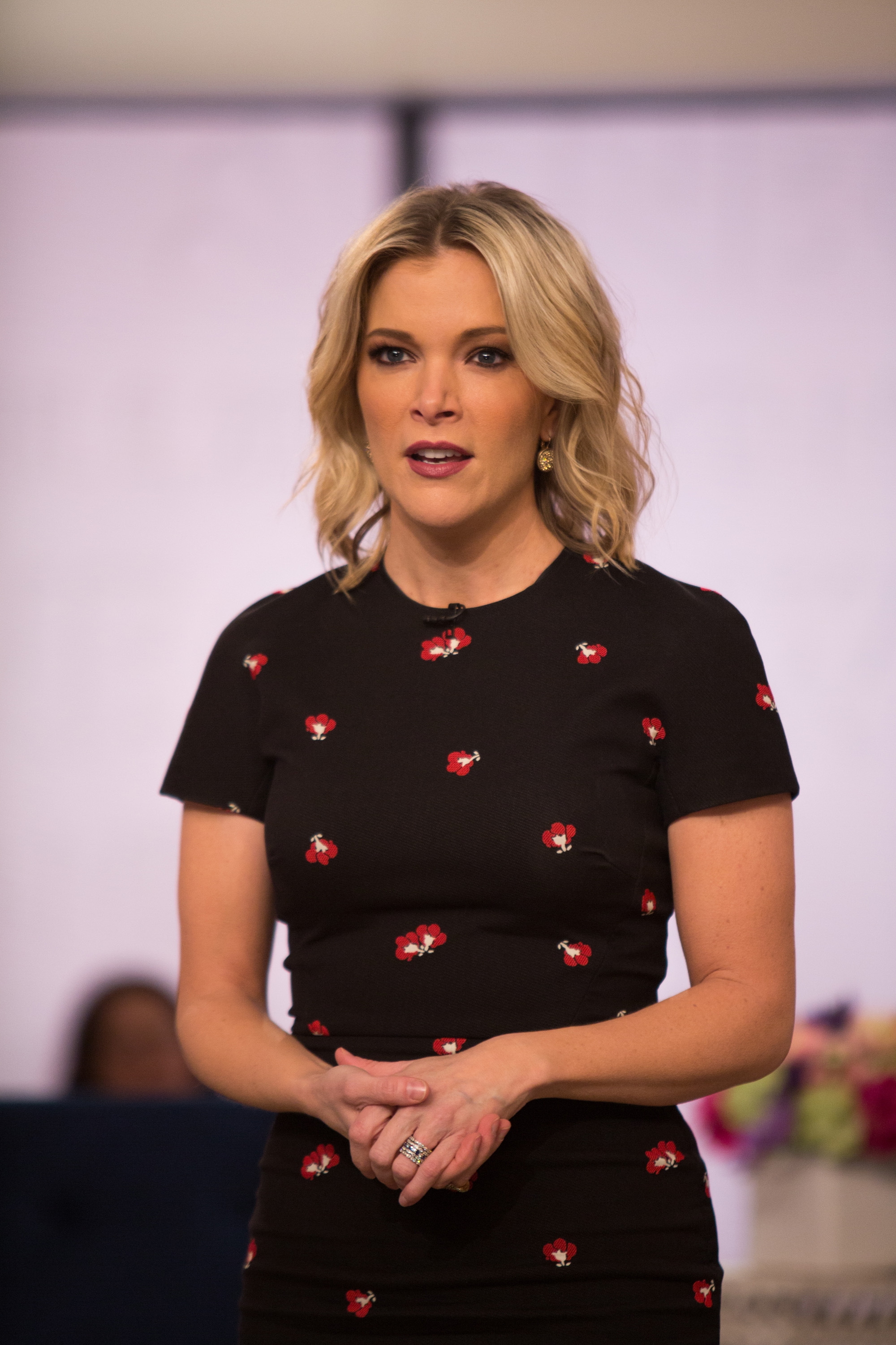 Person in floral-patterned fitted dress, speaking on a news program set