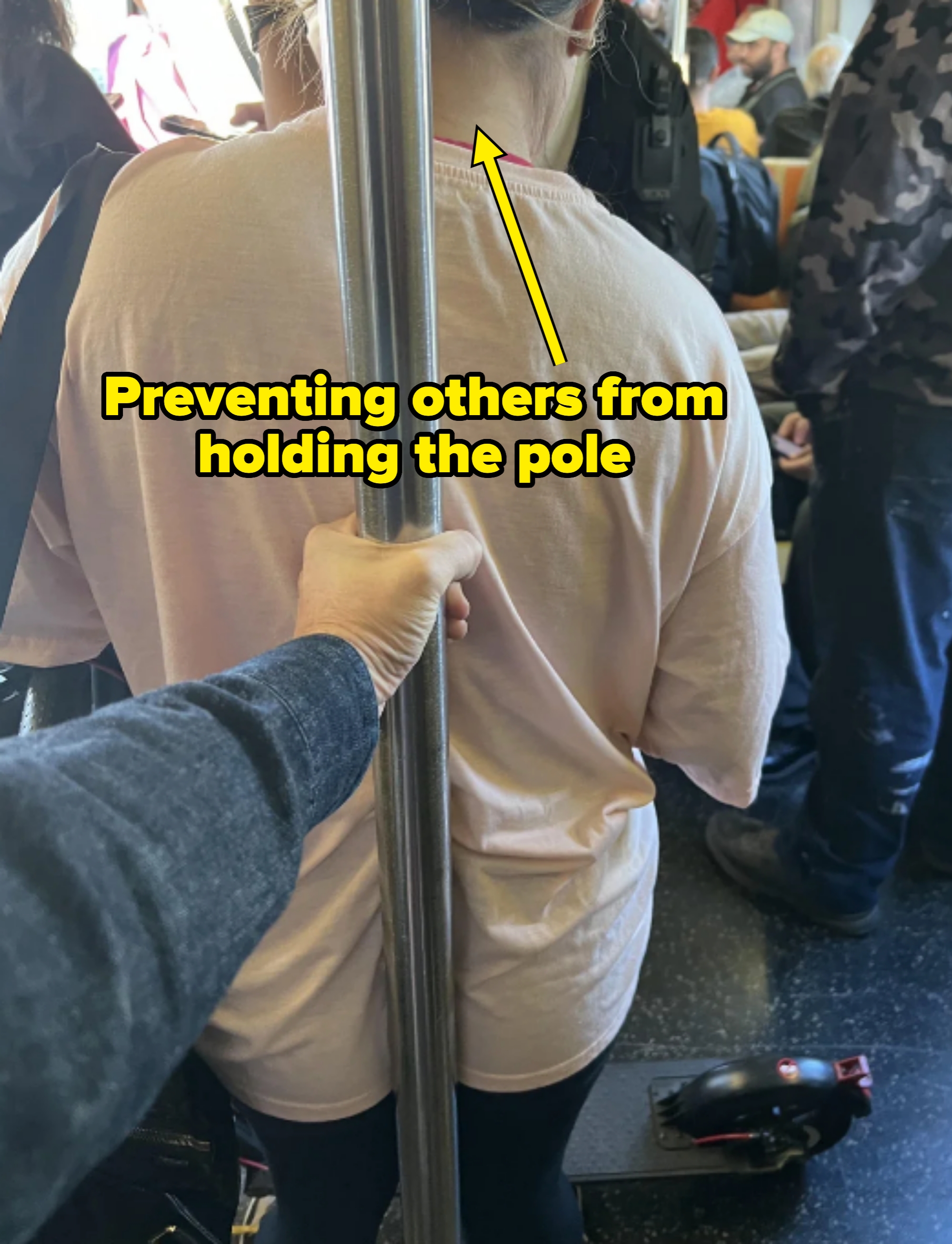 Person standing on a crowded subway, leaning back against a pole, so that no one can hold onto it