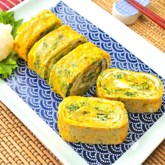 卵焼き風の巻いた卵料理が皿に並ぶ。中に緑の野菜が含まれている。付け合わせに大根おろしとパセリが添えられている。