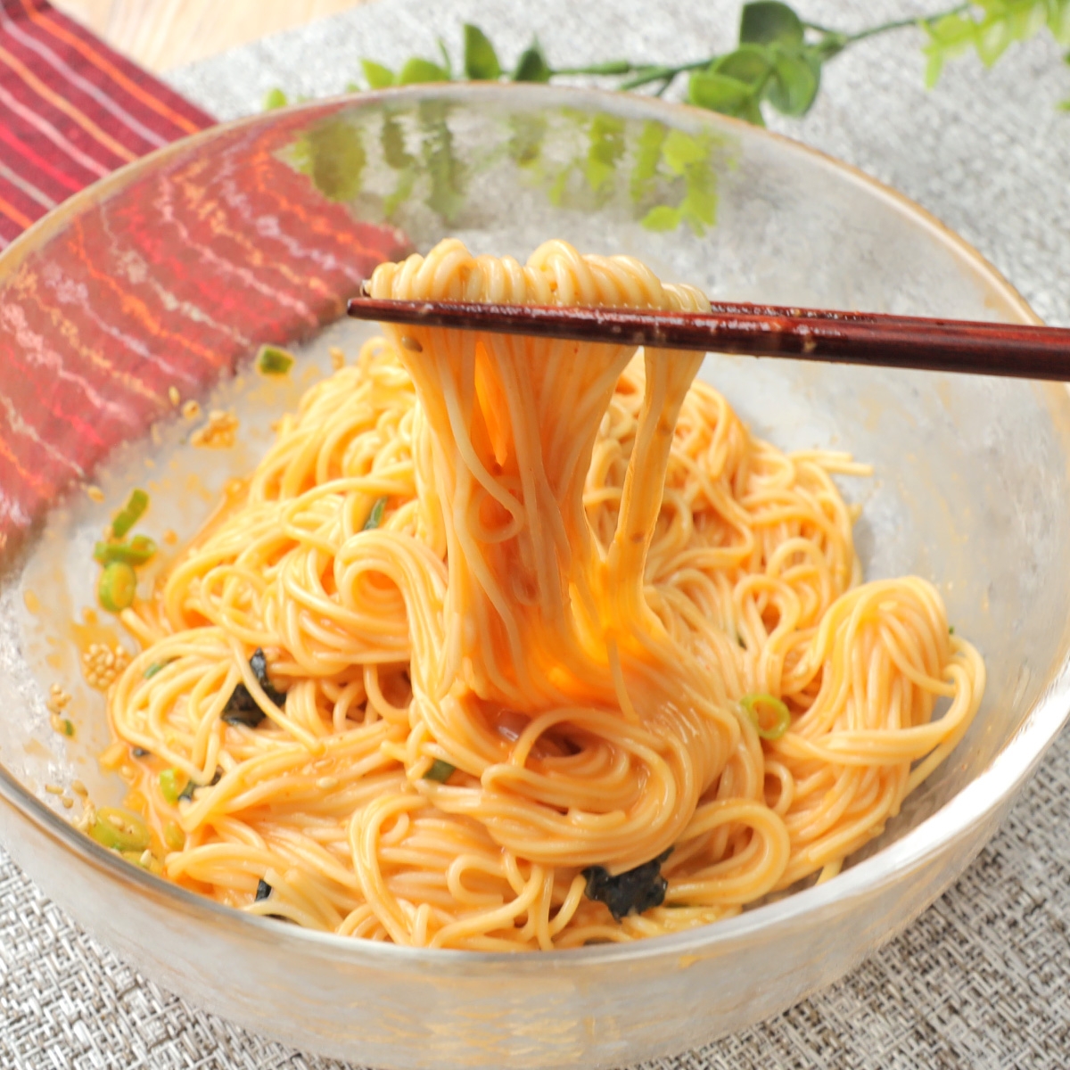 箸で持ち上げられた麺のボウル。ネギと海苔が上にのっており、美味しそうな食事の様子。