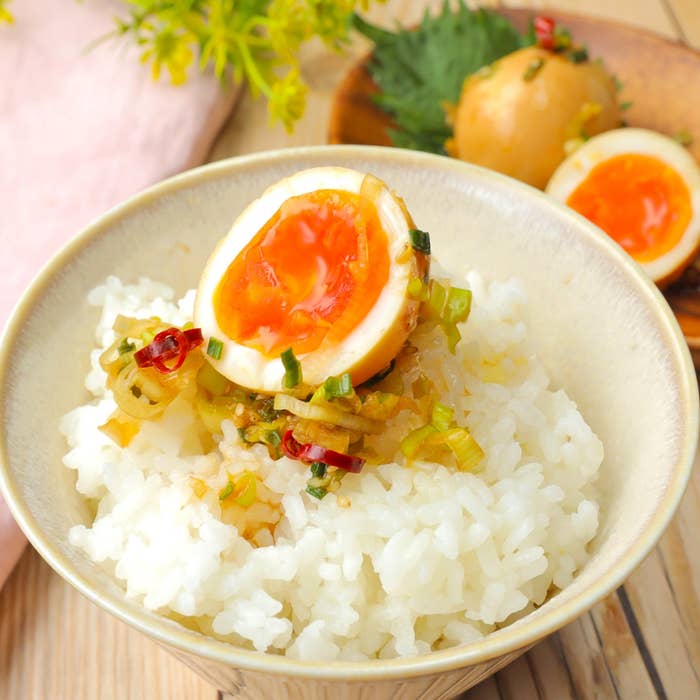 半熟煮卵が載ったご飯、おろし生姜と刻み野菜を添えて。背景にもう一つの半熟煮卵があります。