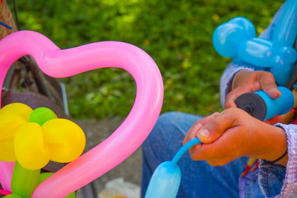 Person inflating colorful balloon animals outdoors, surrounded by grass.