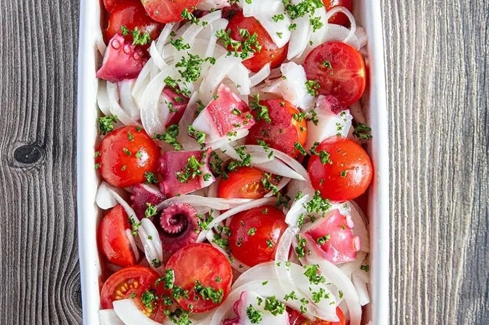 トマト、タコ、タマネギのスライスとパセリをのせたサラダが白い皿に盛られている。