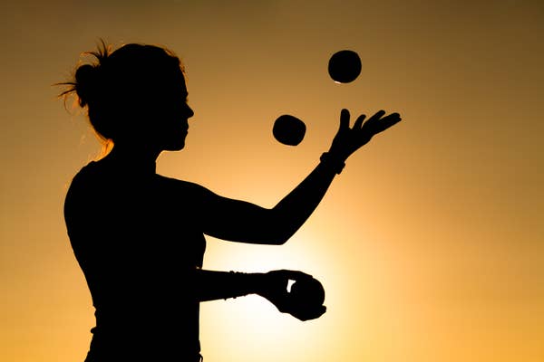 Silhouette of a person juggling three balls against a sunset background.