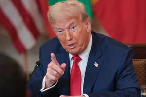 人物はスーツを着用し、指を指しながら会話をしています。室内での公式なイベントの様子です。