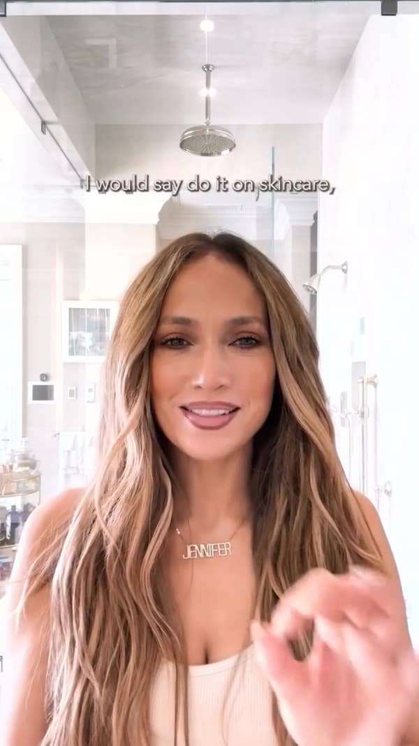 Person with long wavy hair, wearing a tank top and necklace, in a bright room. Text: \"I would say do it on skincare.\"