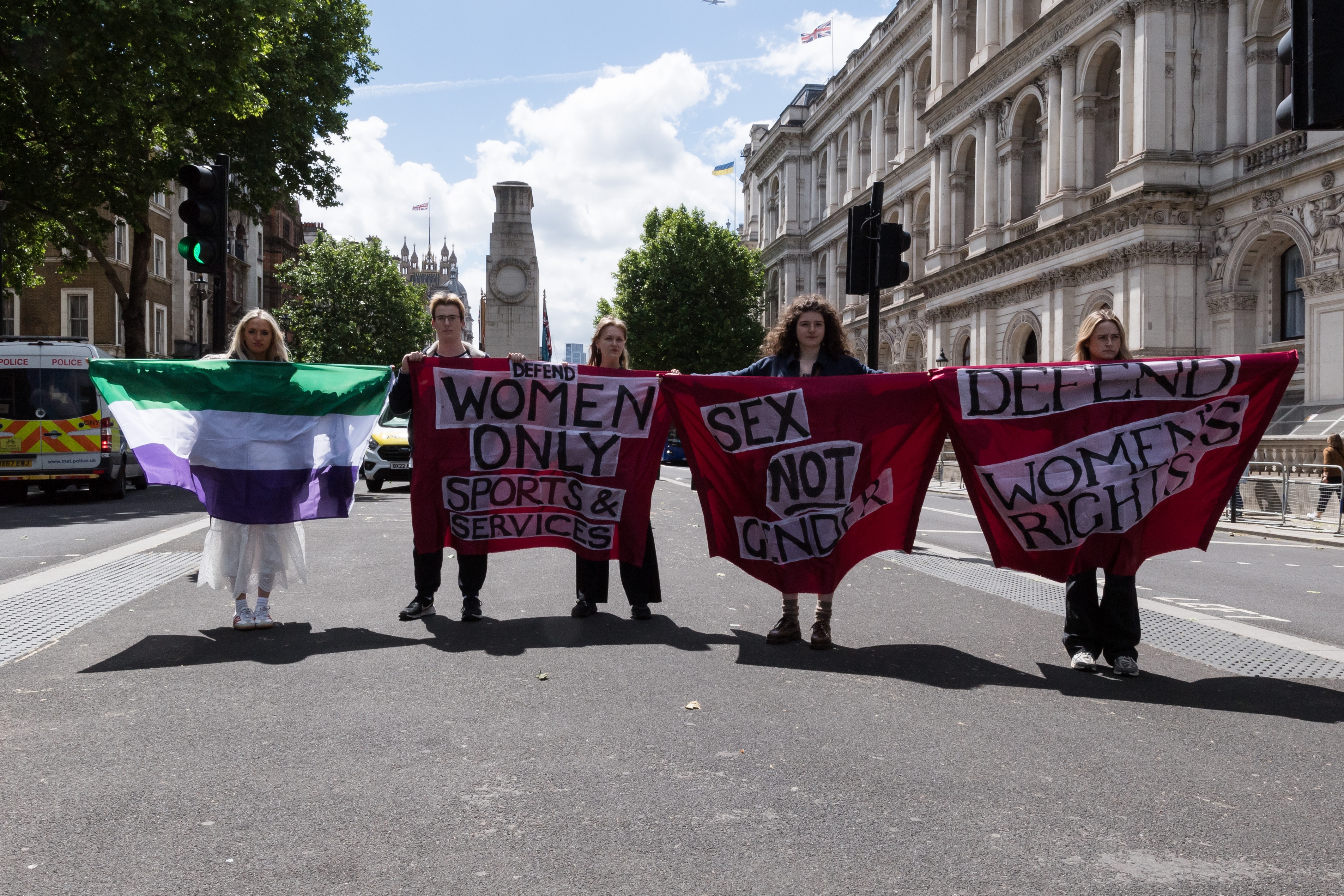 Group of individuals holding protest banners defending women&#x27;s rights and spaces on a city street