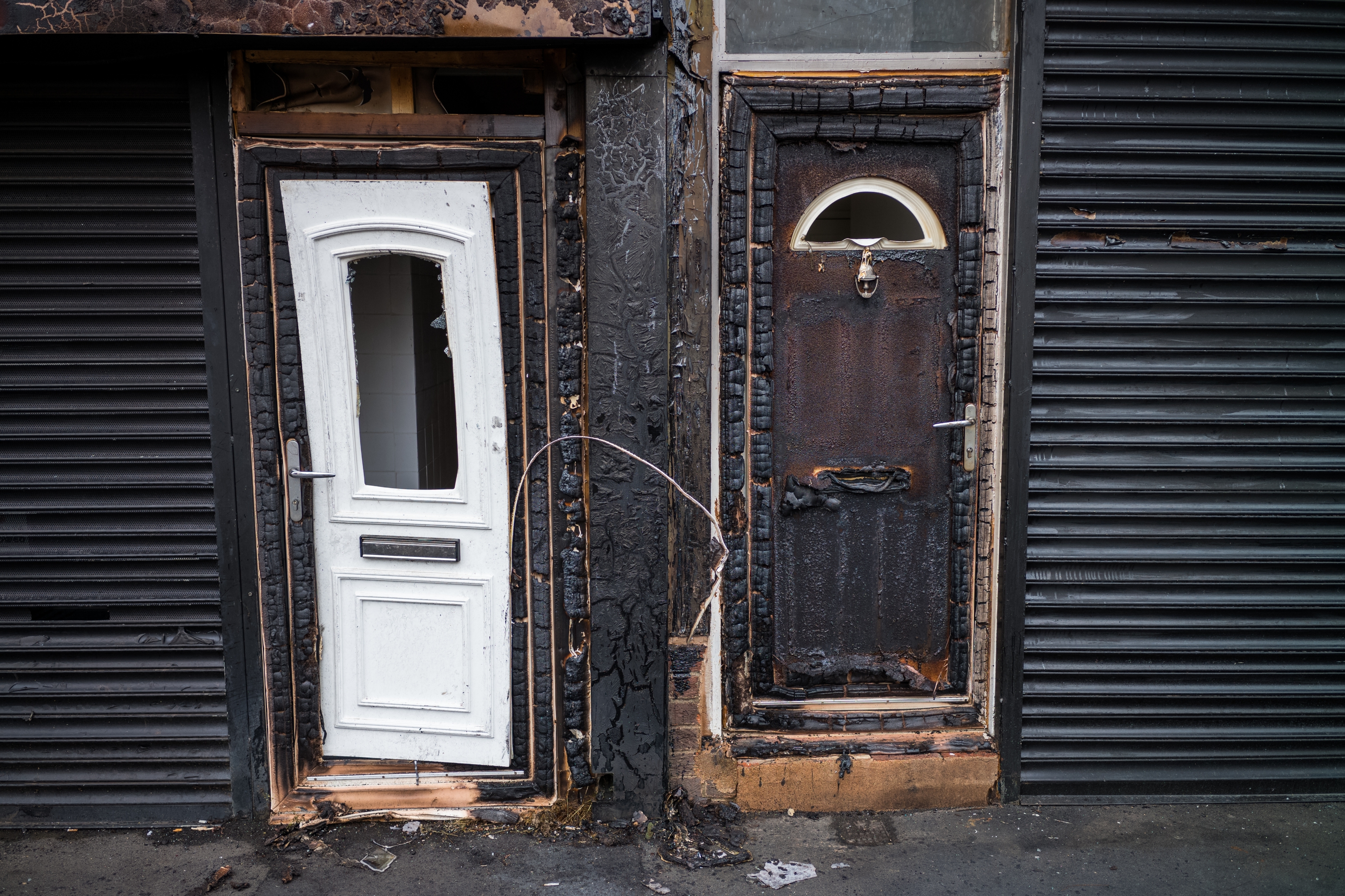 Two adjacent doors, one white and one charred, amidst fire damage. The image may illustrate the aftermath of a fire incident