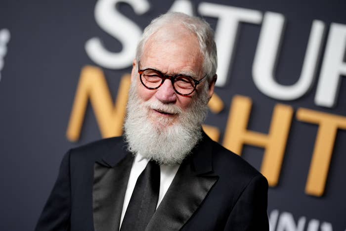 Man with glasses and a white beard in a tuxedo on a formal event backdrop