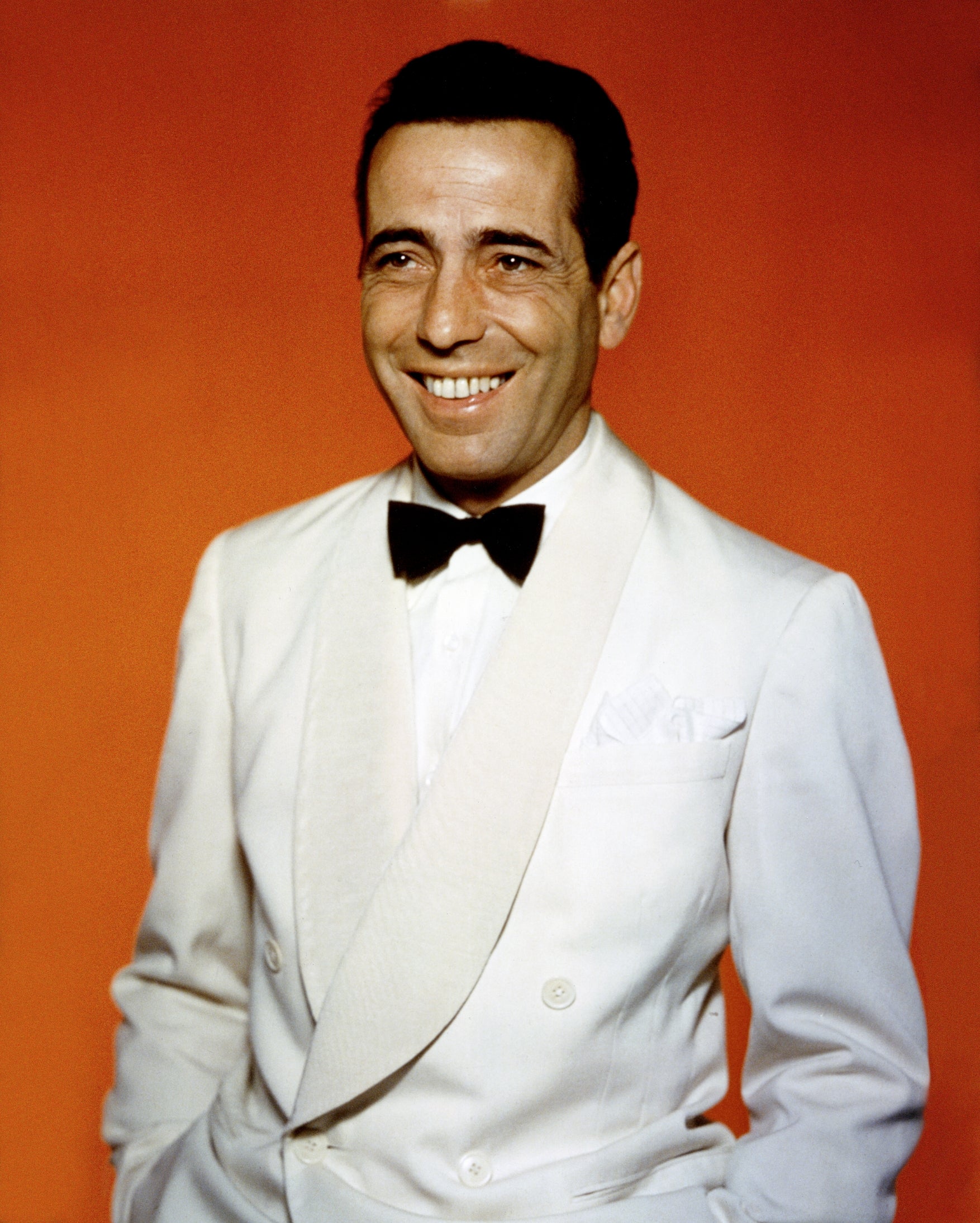 Person successful a classical achromatic tuxedo and achromatic bow tie, smiling against an orangish backdrop