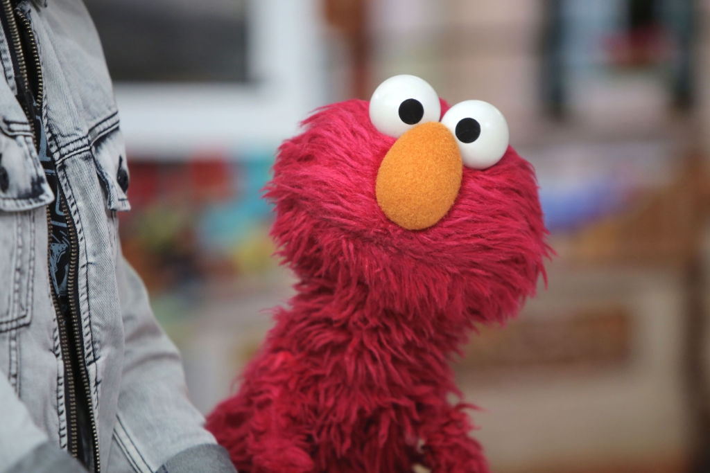 Elmo from Sesame Street is looking up with a curious expression beside someone in a denim jacket