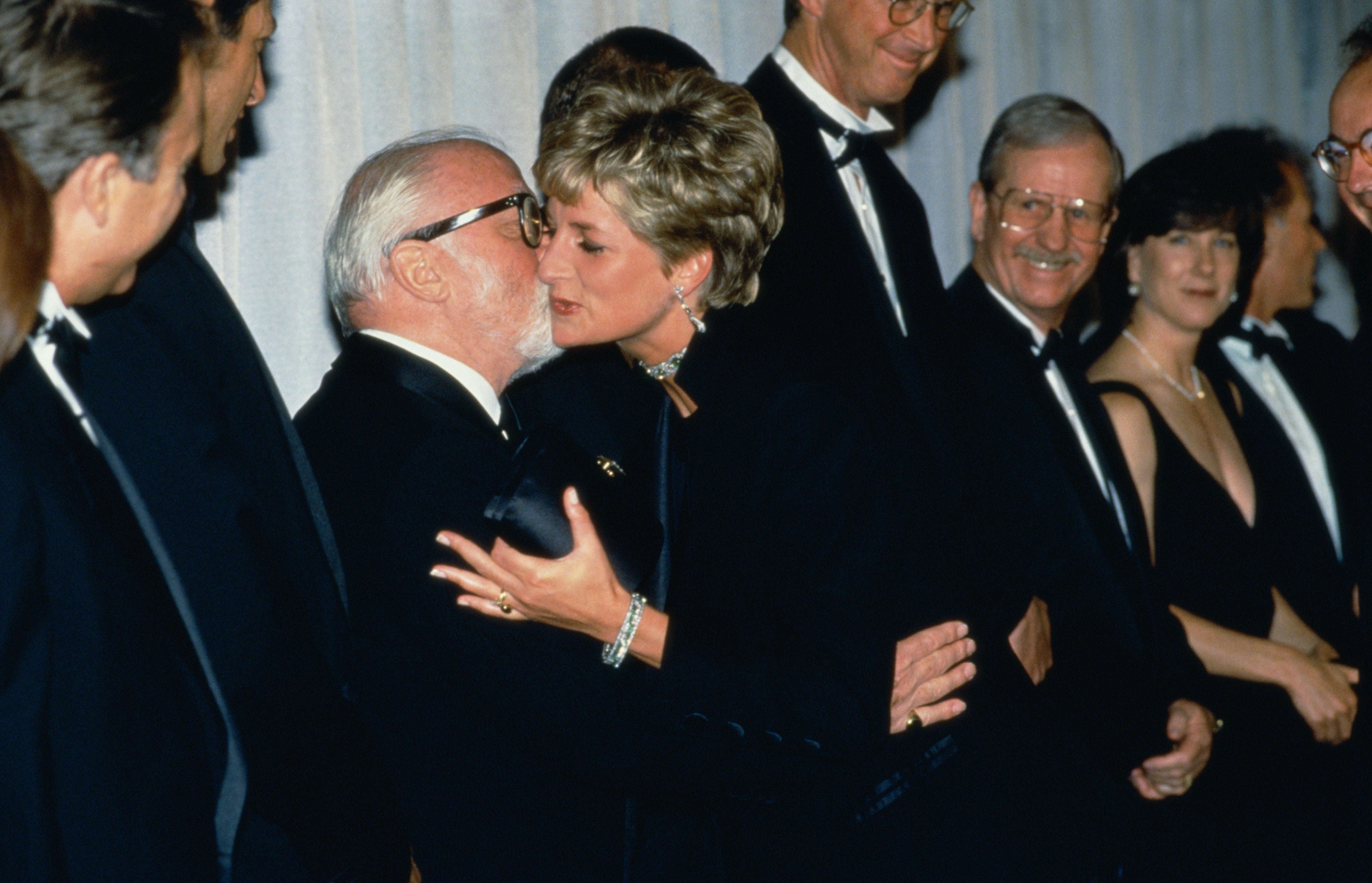A pistillate successful elegant evening deterioration greets an older antheral with glasses astatine a ceremonial event. Others successful ceremonial attire ticker and smile