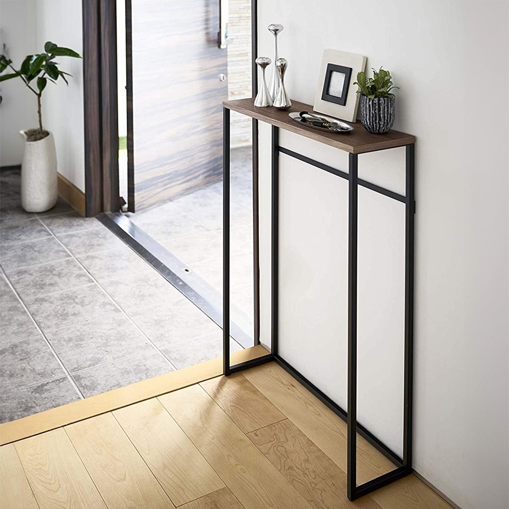Modern entryway with a slim console table holding decor items and a small plant near an open door