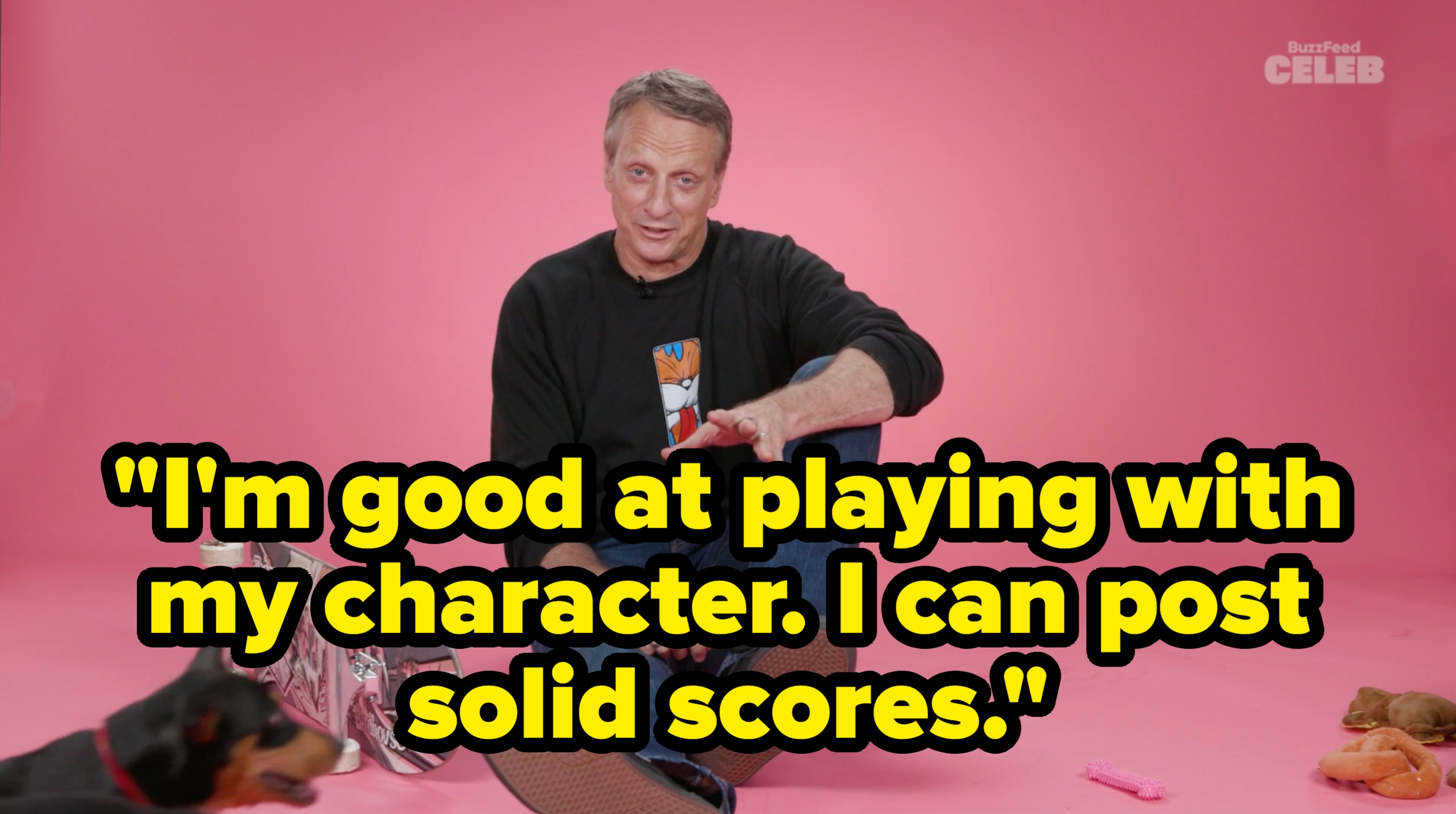 A man sits casually on the floor with a skateboard and toys nearby, suggesting a relaxed, informal interview setting