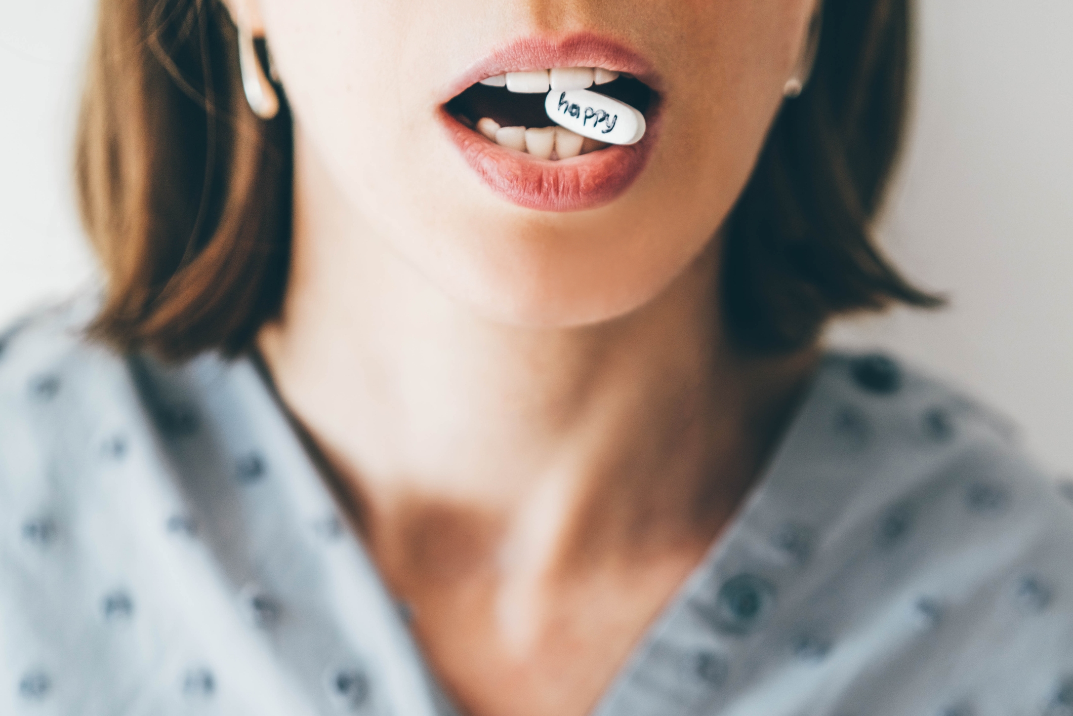 Woman partially visible holding a small "happy" paper piece between teeth, wearing hoop earrings and polka dot top
