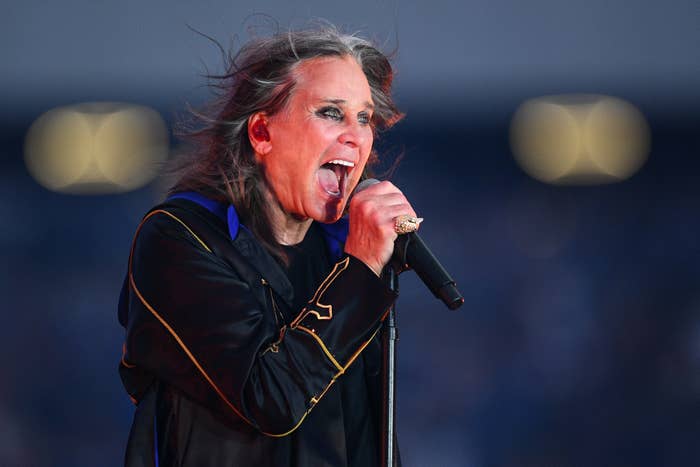 Singer passionately performing on stage, wearing a bold black outfit with gold accents and holding a microphone