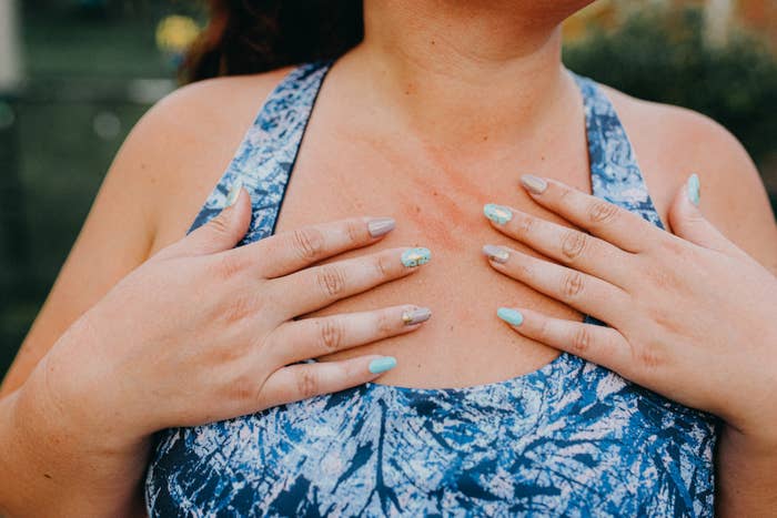 Person with painted nails has hands on chest, wearing a patterned top