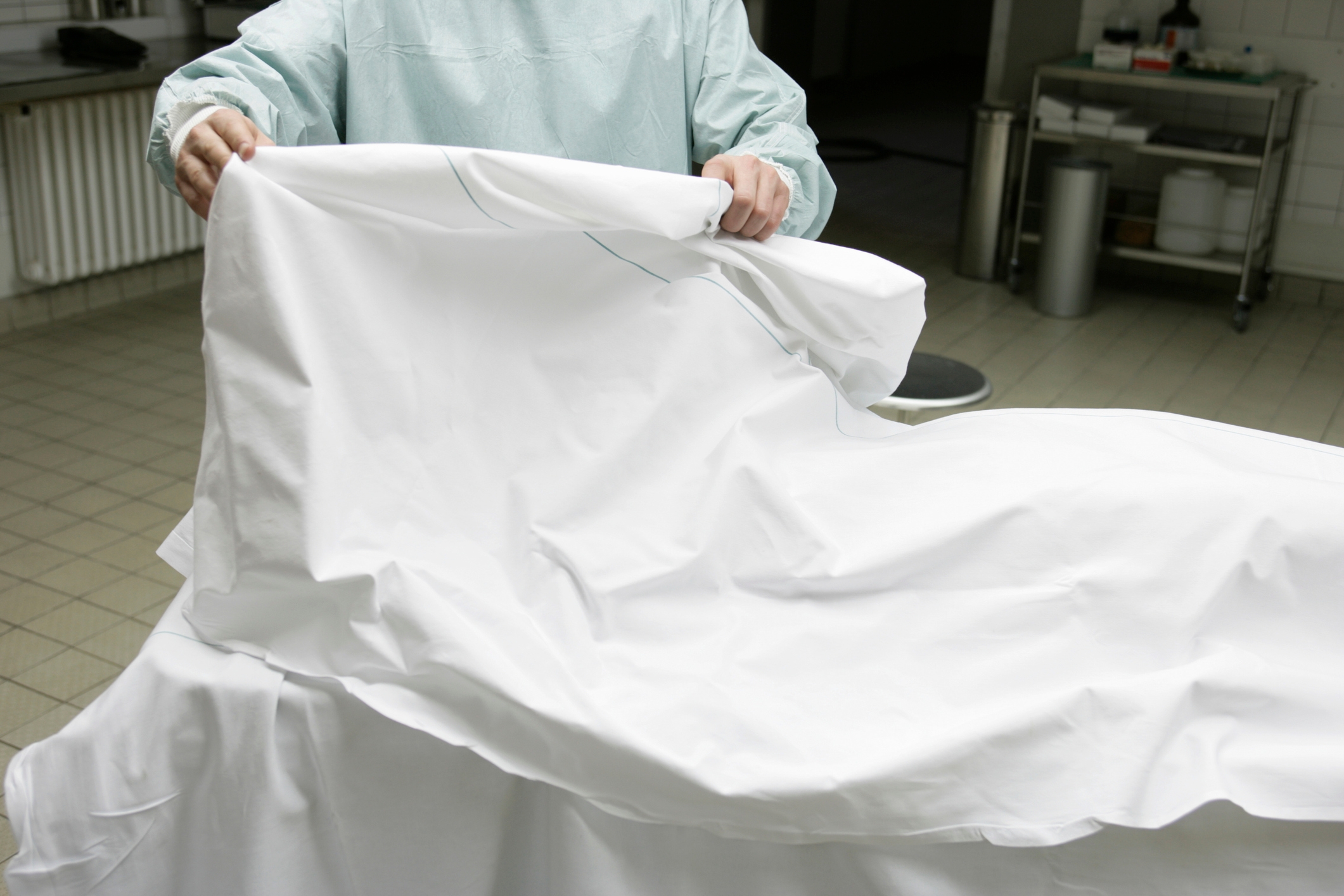 Person in scrubs covering a hospital stretcher with a white sheet in a sterile medical environment