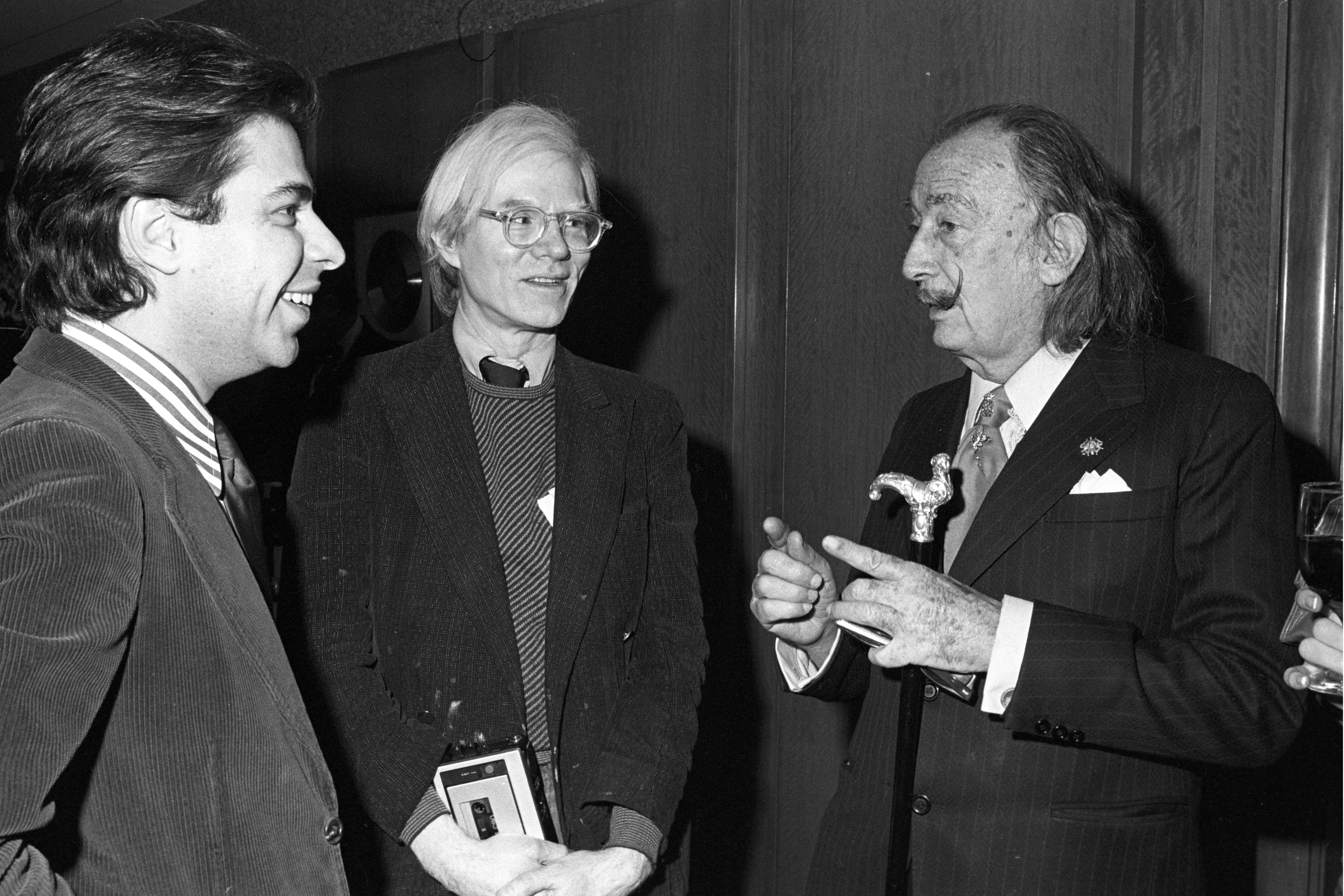 Three men successful ceremonial attire are having a conversation. One holds a decorative object. The ambiance is lively and engaged