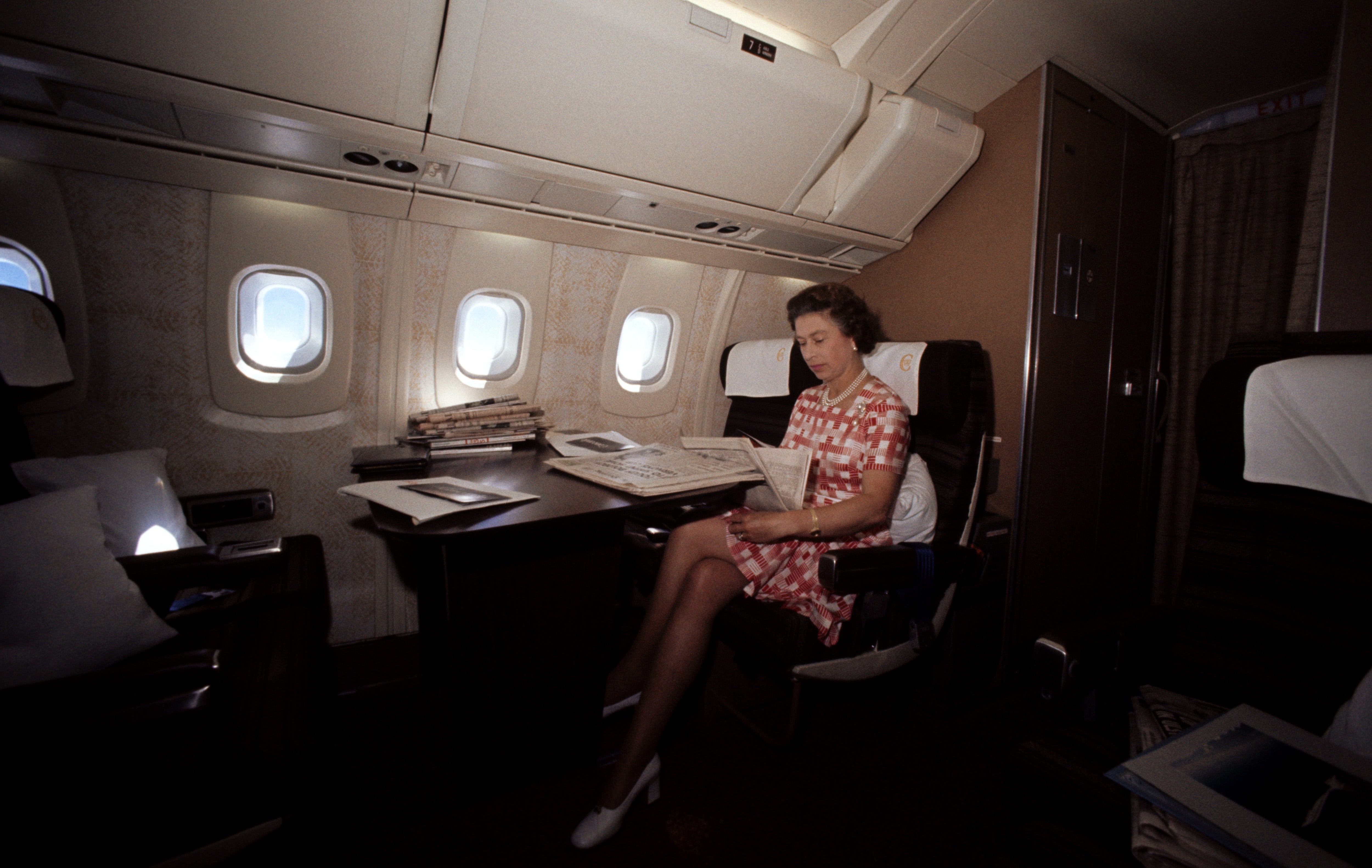 A pistillate successful a patterned formal reads a paper aboard a backstage jet, with bare seats and papers astir her
