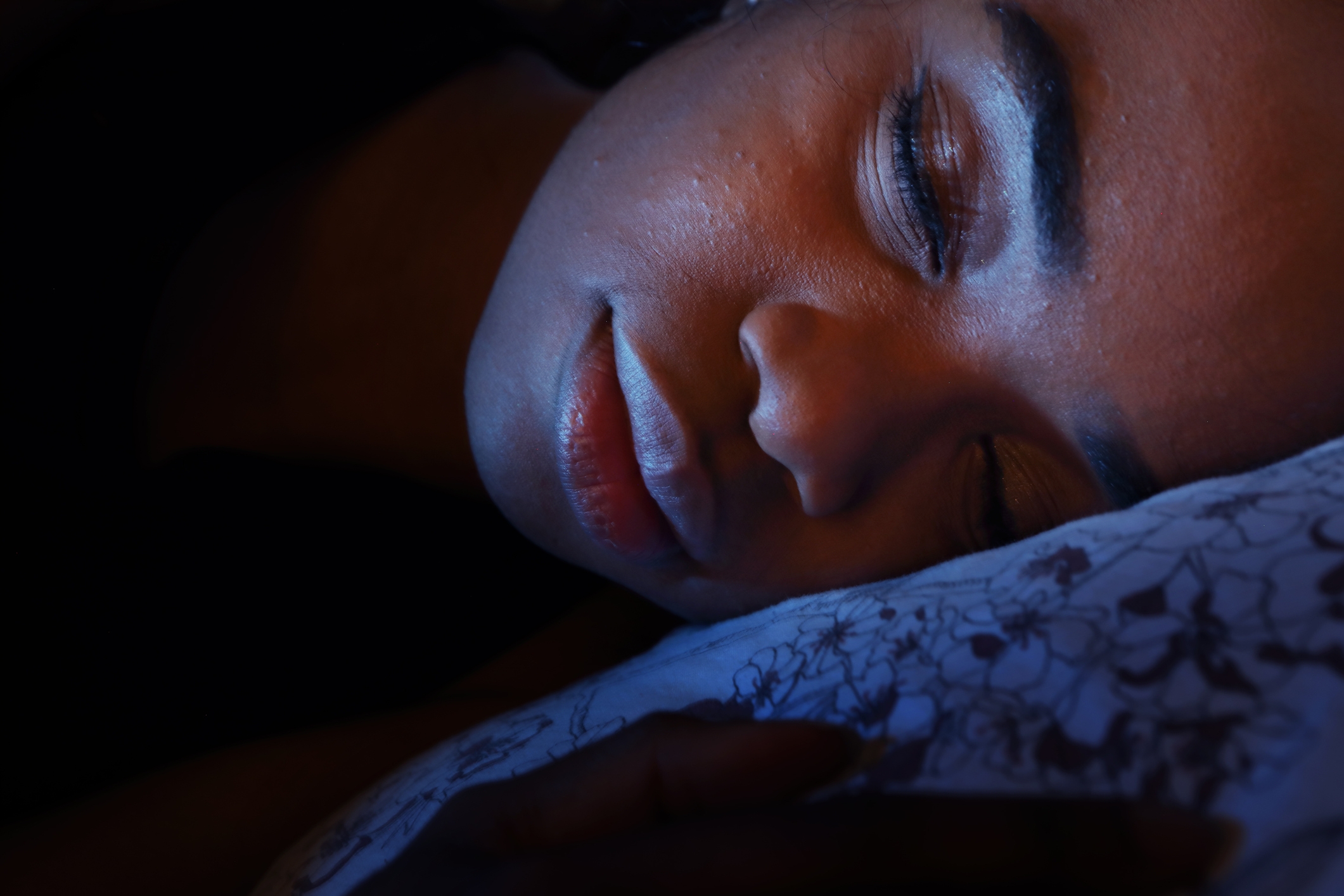 Person peacefully sleeping with their head resting on a patterned pillow, illuminated by soft light