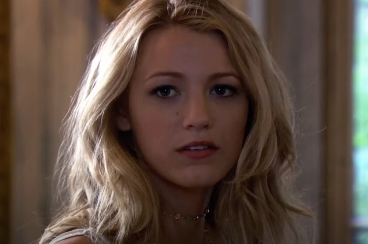 A person with long, wavy hair looks towards the camera with a neutral expression, wearing a choker necklace